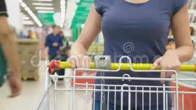 超市里的一个女人正从柜台边经过篮子。 一个女人在超市里走来走去，特写镜头。